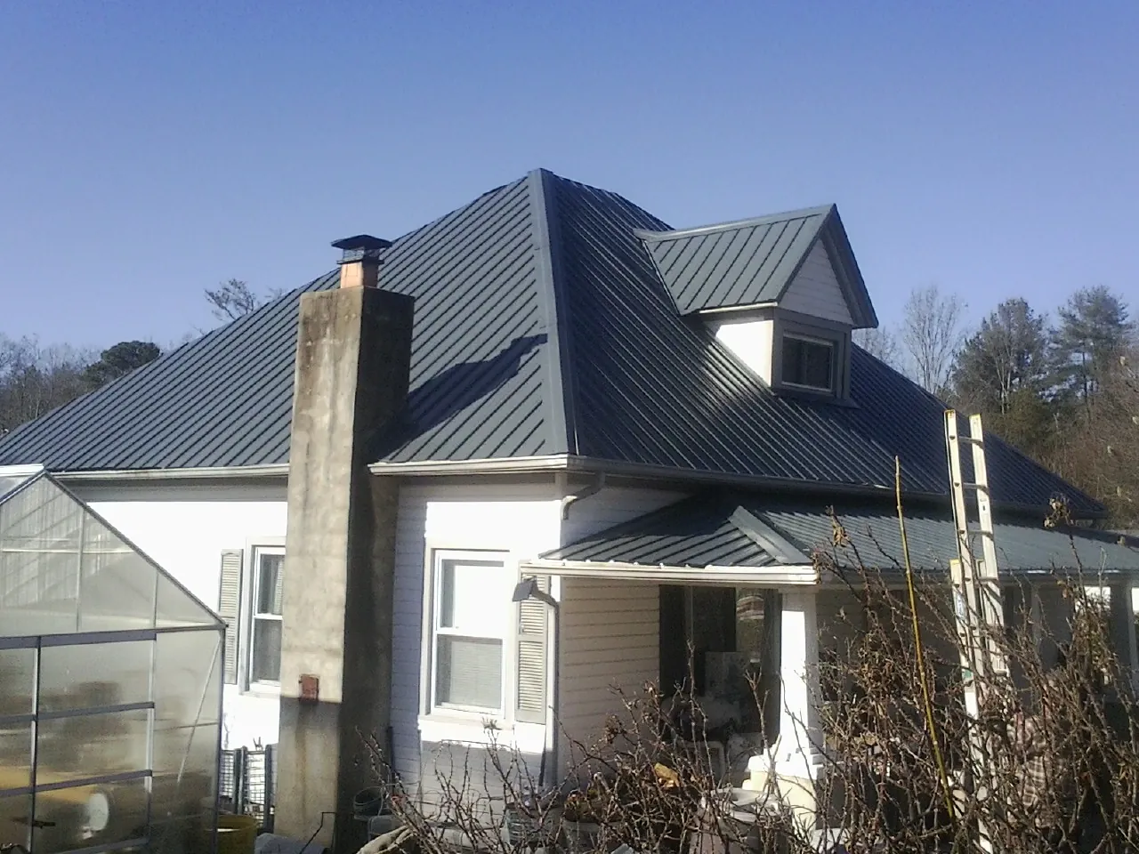 Dark blue standing seam metal roof on a white farmhouse with dormer — Slate & Tile Roof Repair by Roofing Brothers in Old Fort