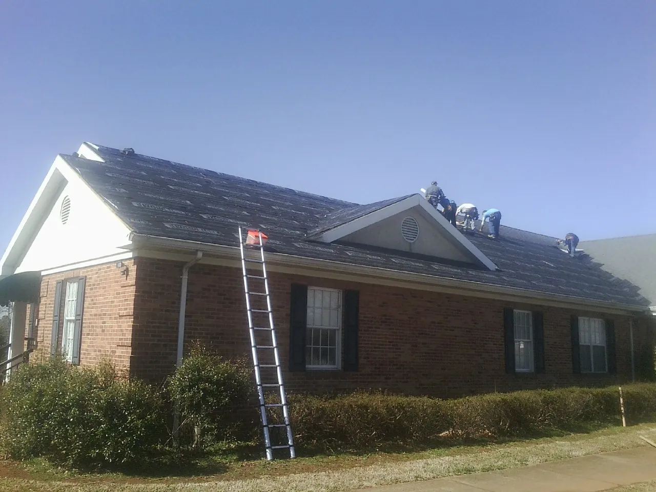 Crew tearing shingles off a brick ranch roof with a ladder set — Emergency Roof Repair work by our crew in Old Fort