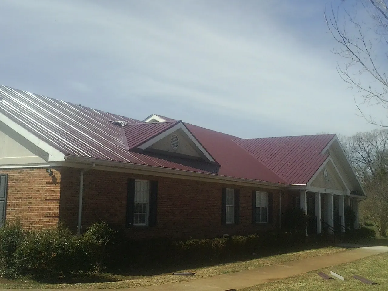 Red metal roof with gabled entries on a long brick building, from a Hail Damage Roof Repair job in Old Fort
