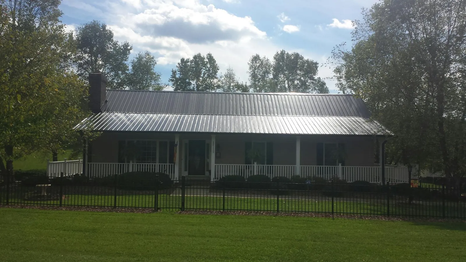 Gray metal roof on a brick ranch with a full width front porch — Gutter Guard Installation work by our crew in Old Fort