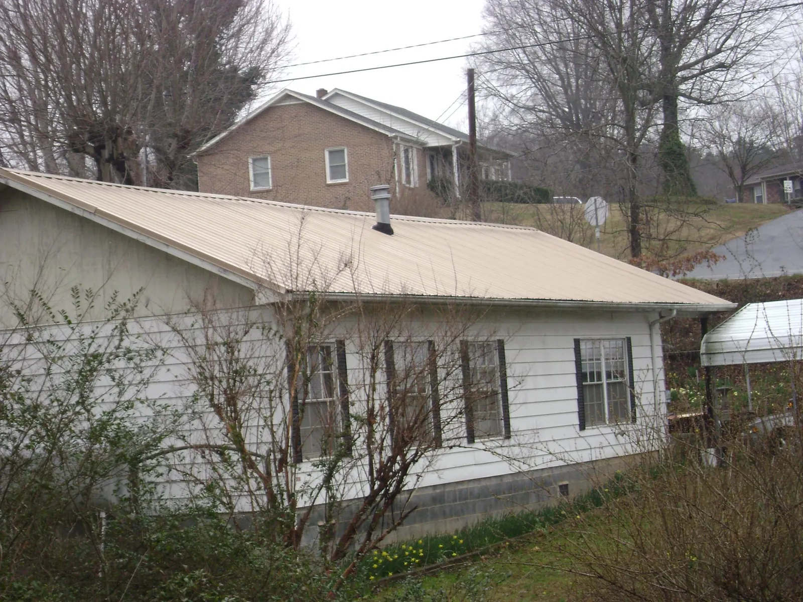 Tan metal roof on a white sided house set into a hillside — Commercial Roofing by Roofing Brothers in Old Fort